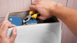 A person is fixing a toilet with pliers.