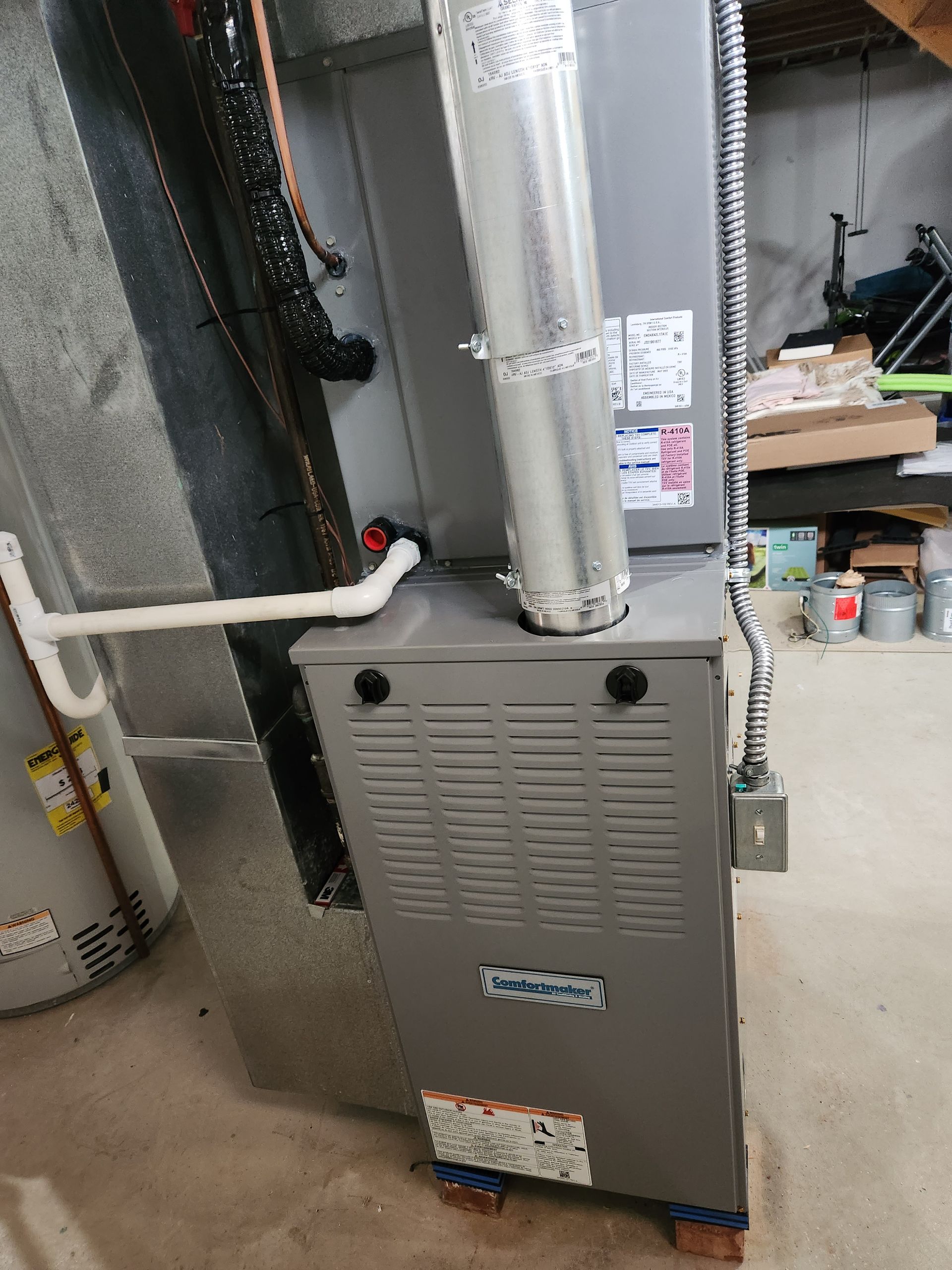 A gray furnace is sitting in a basement next to a pipe.