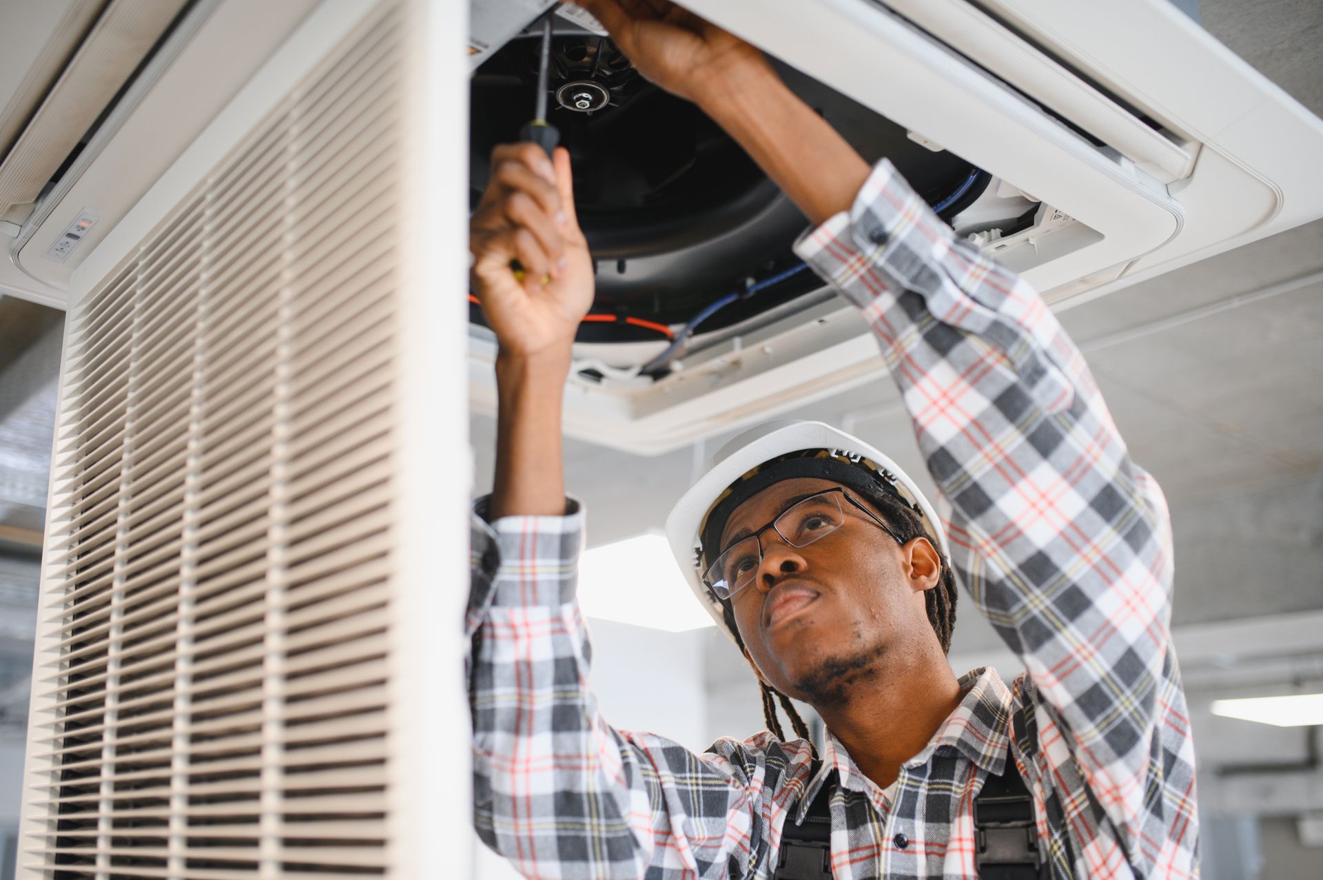 An HVAC technician servicing a ceiling-mounted air conditioning unit using a screwdriver
