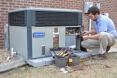 A man is working on an air conditioner outside of a brick building.