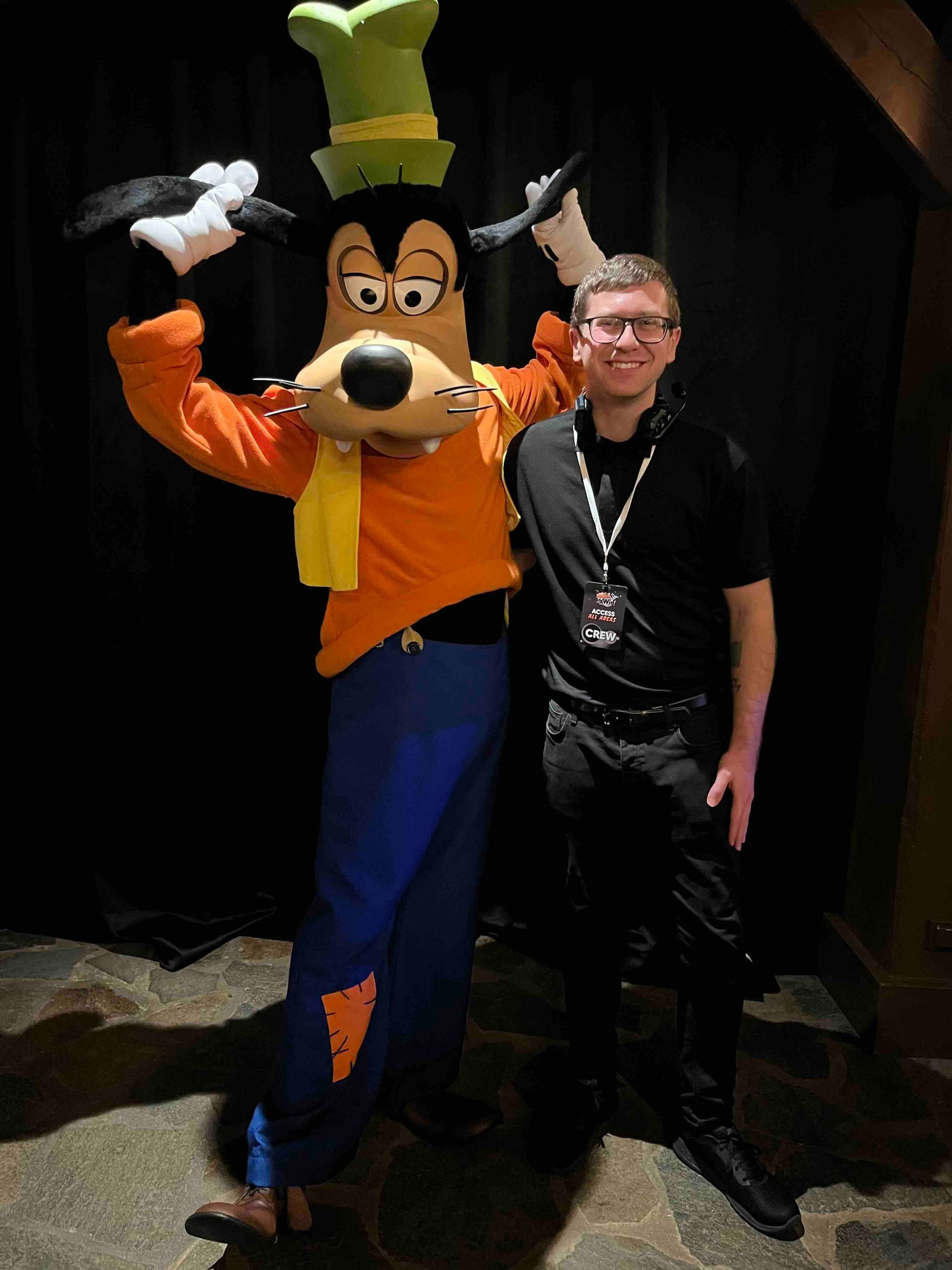 Goofy poses with a man wearing glasses at Disney World. Goofy wears orange and blue, man in black.
