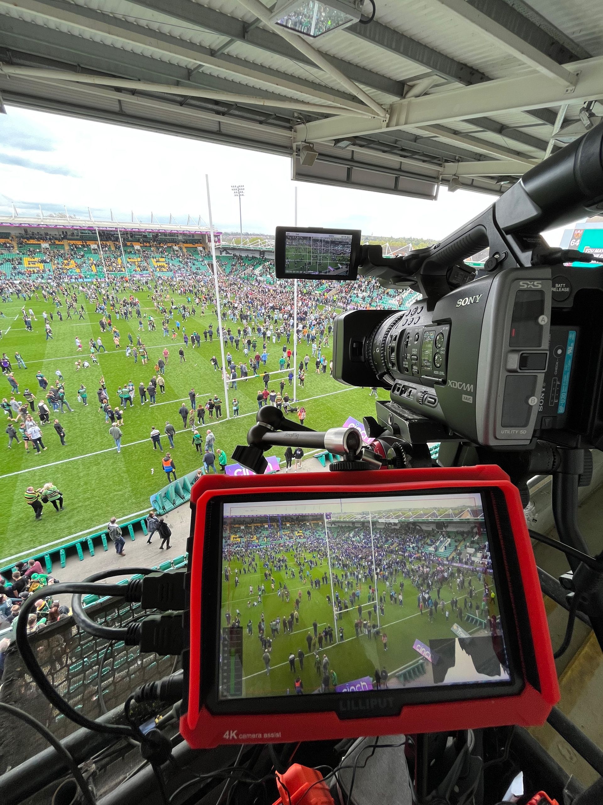 Camera filming a rugby match from elevated position; red monitor shows field with players.