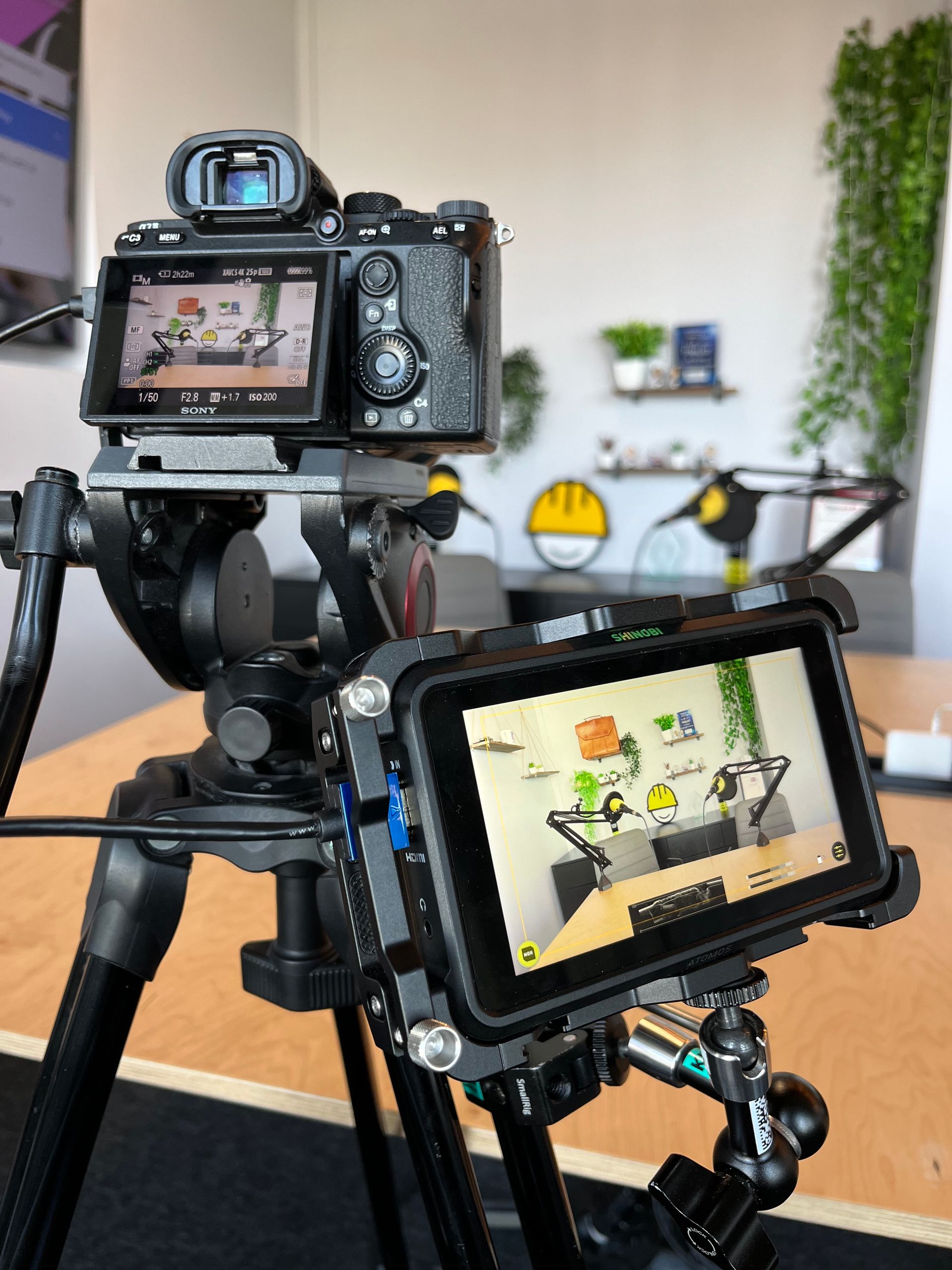 A camera setup on a tripod with an external monitor displaying a podcast set, capturing a live recording.