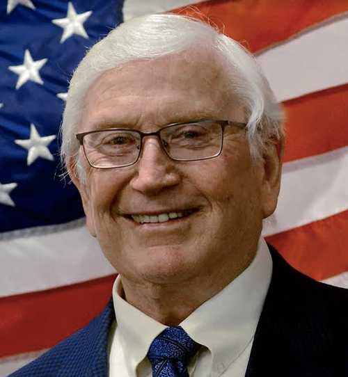 Smiling man in glasses and suit before an American flag backdrop