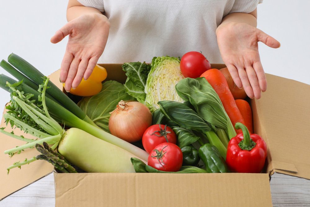 A Person Is Holding A Cardboard Box Filled With Vegetables — Kym Connolly Wellness Coach in Svensson Heights, QLD