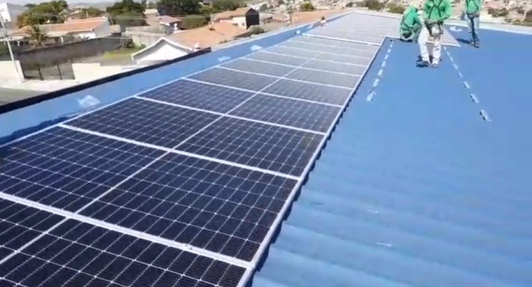 Uma fileira de painéis solares está no topo de um telhado azul.