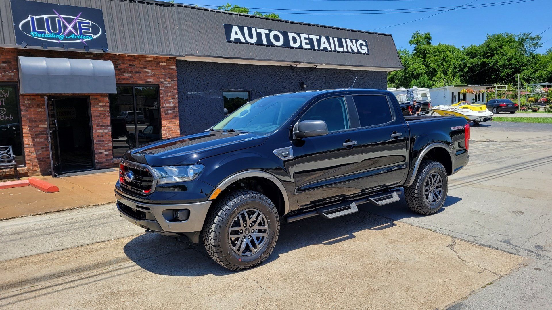 A dark blue Ford Ranger pickup truck parked in front of an auto detailing shop on a sunny day.