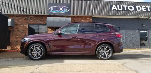 A maroon BMW SUV parked in front of an auto detailing shop with a 