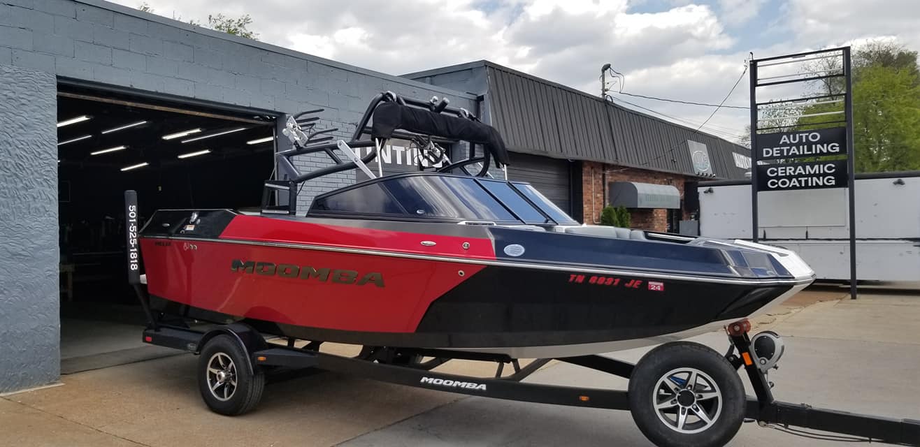 A red and black boat on a trailer in front of a building with a sign.