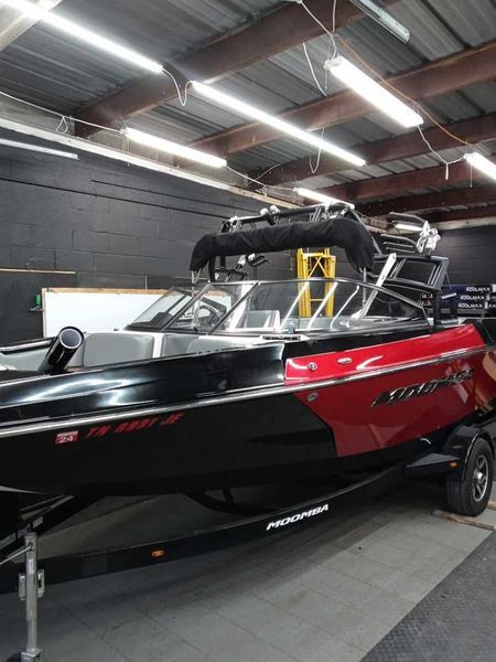 Red and black wake surf boat on a trailer inside a workshop.