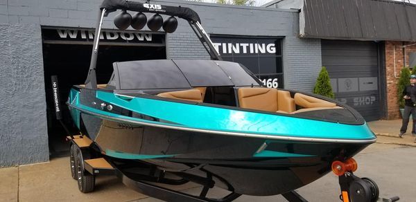 A teal and black motorboat on a trailer outside a window tinting shop.