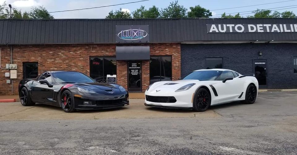 Two Chevrolet Corvettes in front of an auto detailing shop. One is black, one white.