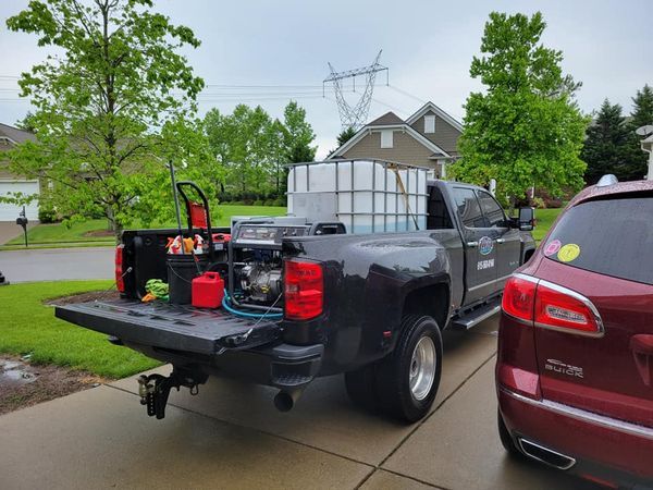 Pickup truck with water tank and pressure washer in driveway.
