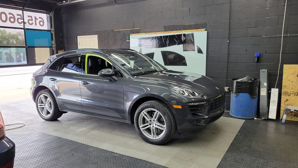 Gray Porsche Macan SUV inside a garage, window tinting in progress.