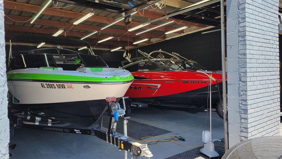 Two boats, one green and one red, are inside a garage, one on a trailer.