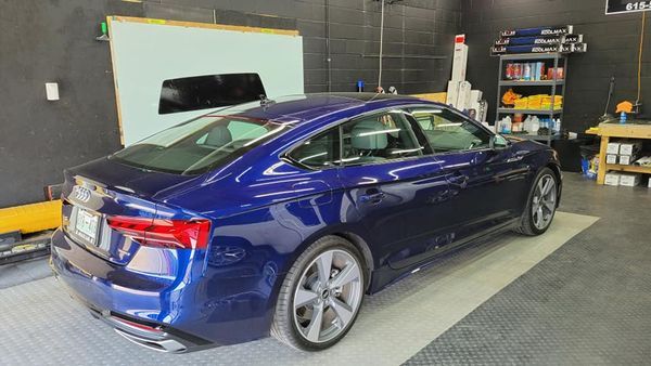 Blue Audi sedan in a garage, window tinting in progress.