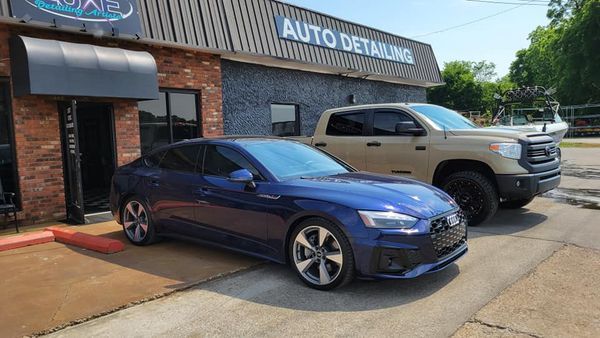 Blue Audi and tan truck parked in front of auto detailing business.