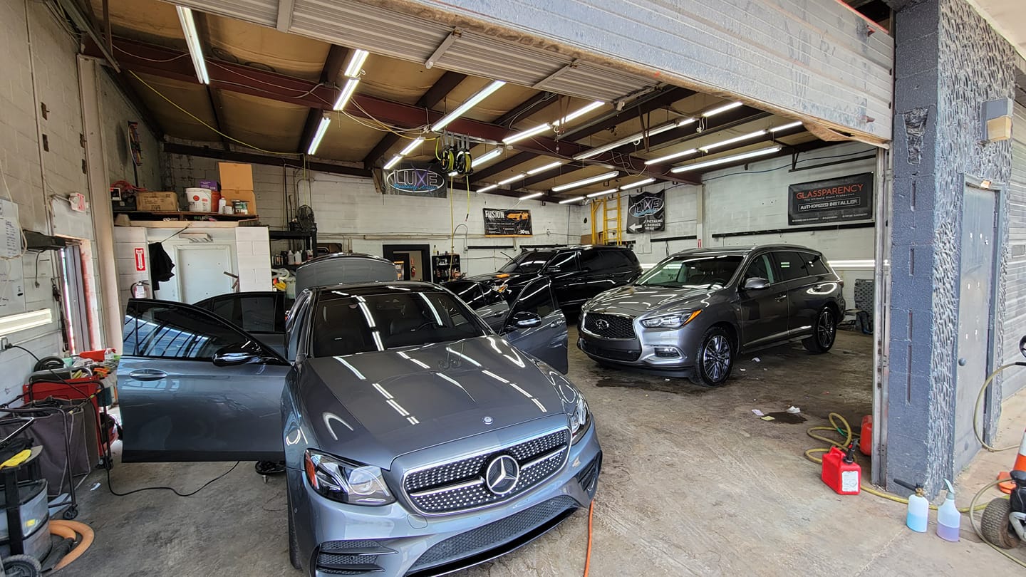 Cars inside a garage: a gray Mercedes, black SUV, and gray SUV, with open garage door and shop tools.