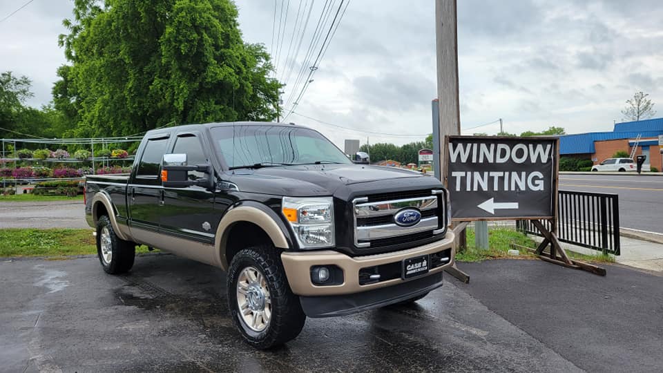 Black and tan Ford truck parked in front of a window tinting sign.
