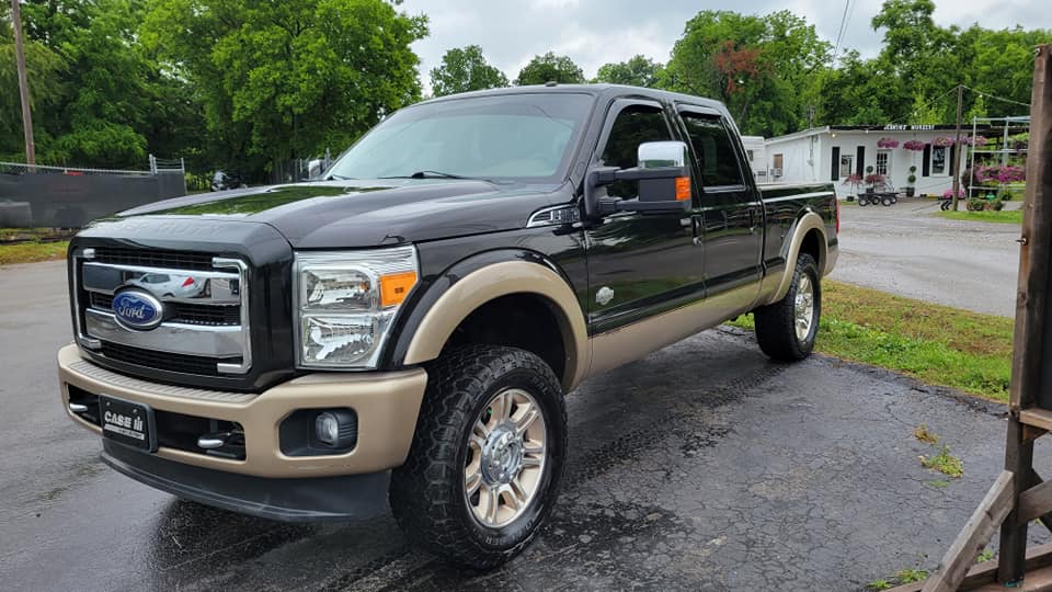 Brown and black Ford F-250 pickup truck parked on wet asphalt, front view.