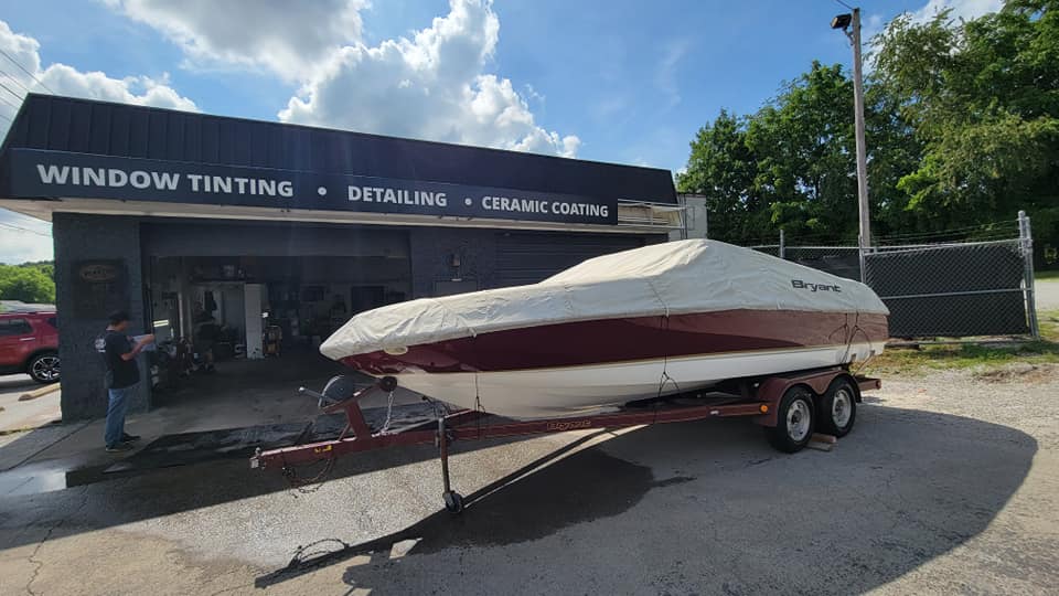 Boat on a trailer in front of a window tinting and detailing business.  Red and white boat, man working.