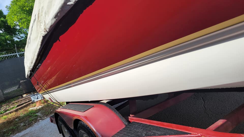 Red and white boat on a red trailer, with a gold stripe and a protective cover.