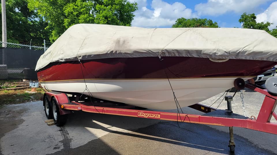 Boat on a red trailer with a white hull and maroon stripe, covered by a beige tarp.