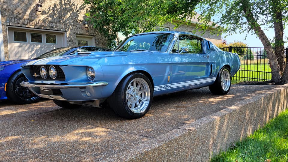 Light blue classic Ford Mustang with white stripes, parked on driveway.
