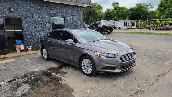 Gray Ford Fusion parked in front of a dark building with tinted windows, on a paved surface.