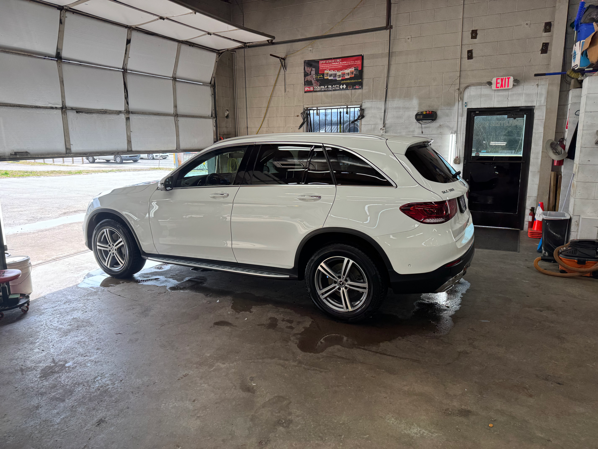White SUV inside a garage; wet floor, open bay door to the left, black door to the right.