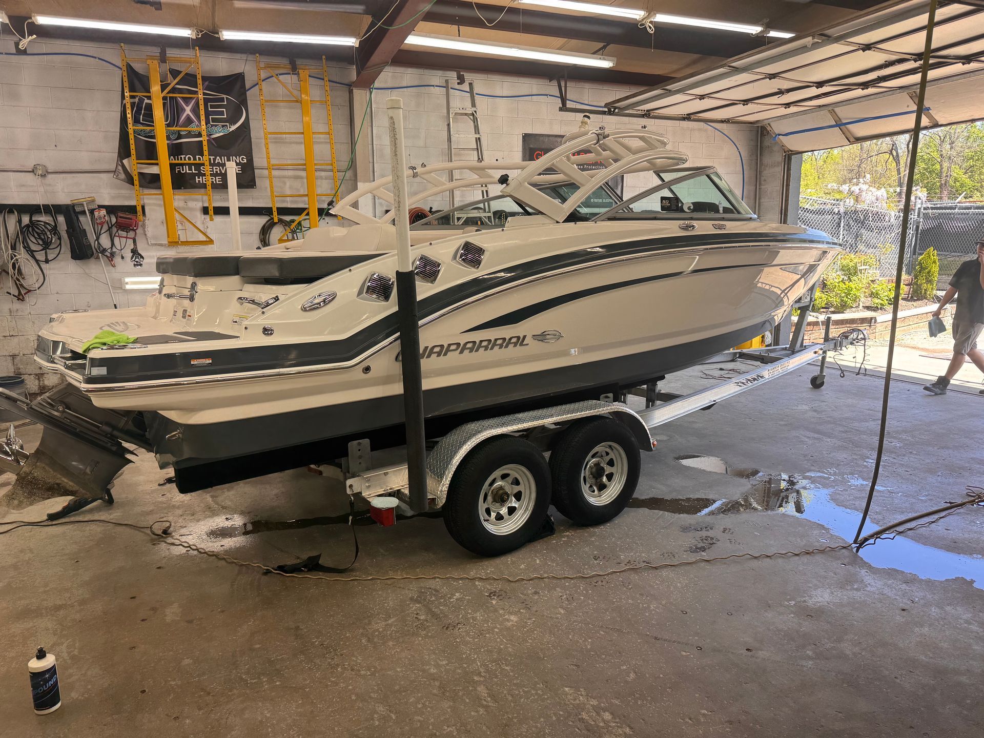 Boat on trailer in a garage. Beige and black boat, two axel trailer, person walks nearby.
