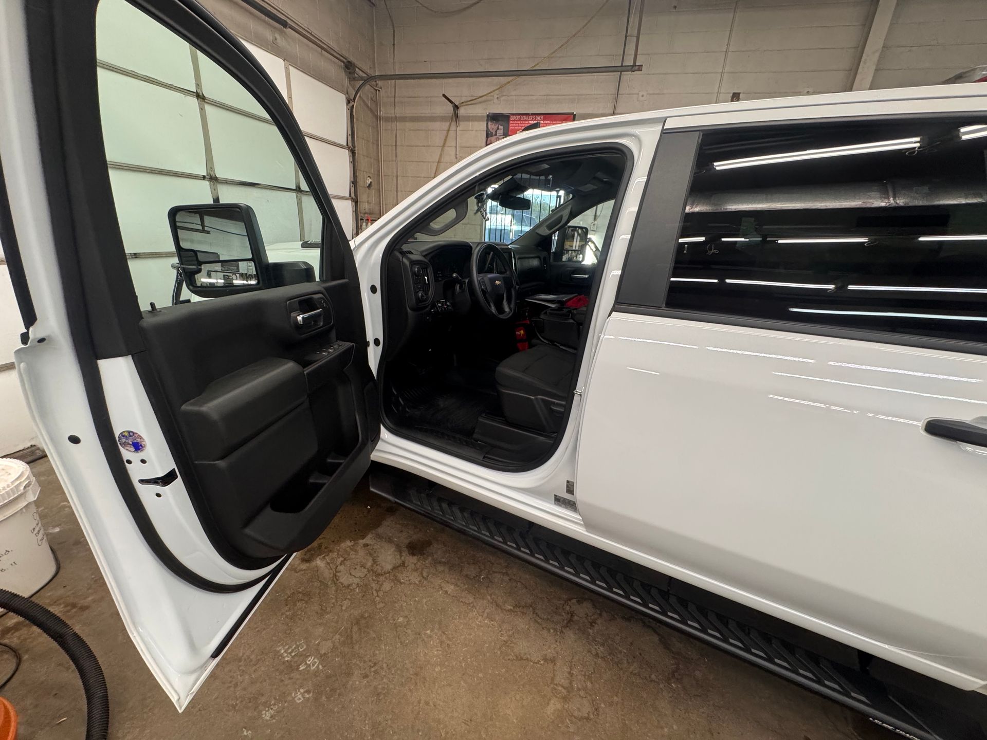 White pickup truck with driver's side door open, revealing black interior and side mirror, parked inside a garage.