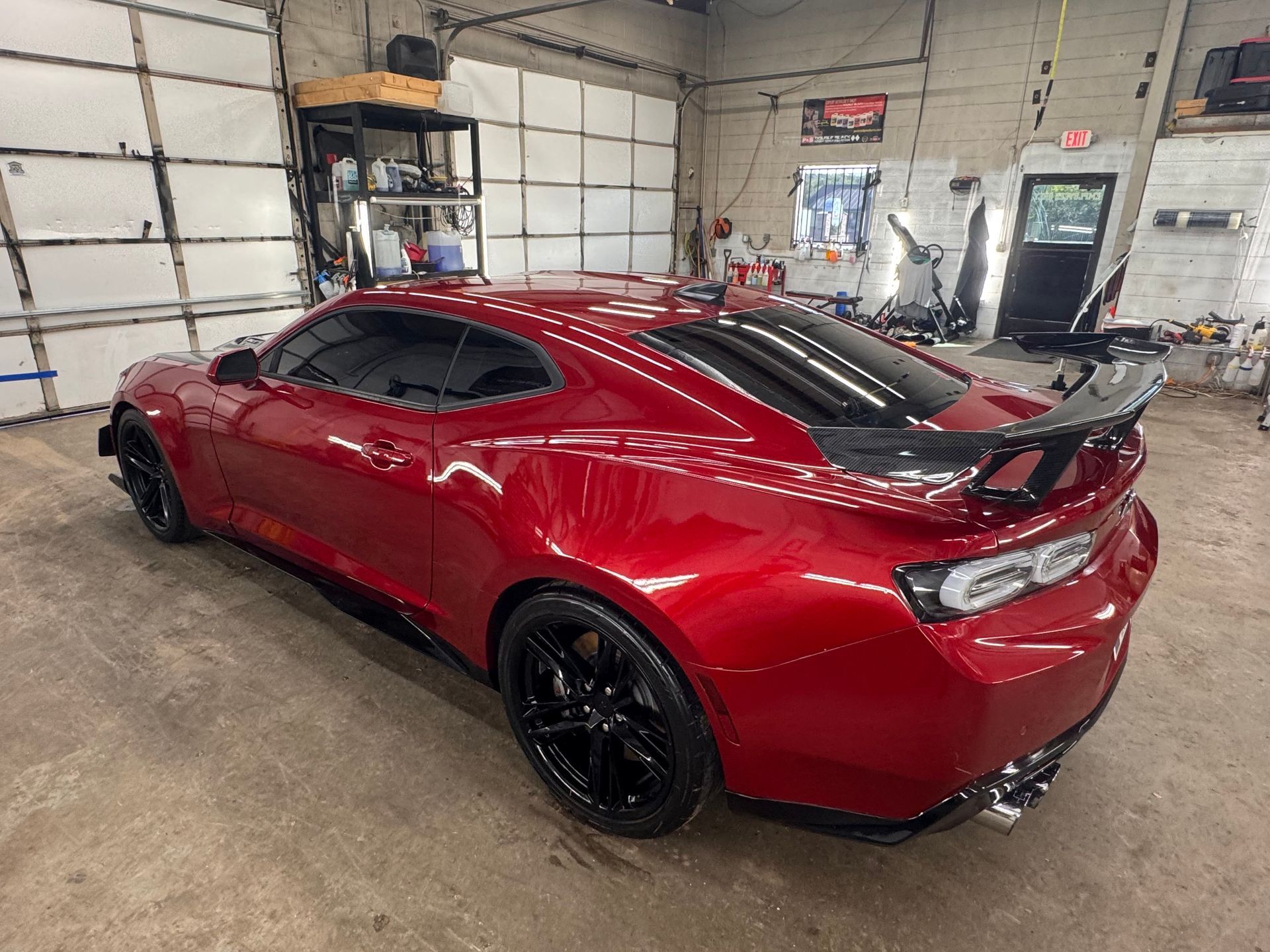 Red sports car with black wheels and spoiler inside a garage.