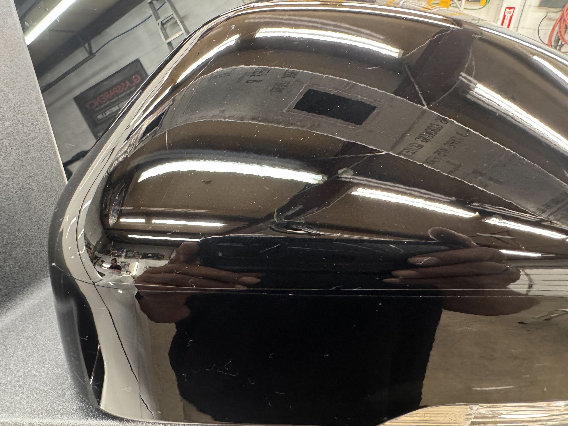 Close-up of a glossy black motorcycle gas tank reflecting surroundings and a person taking the photo.