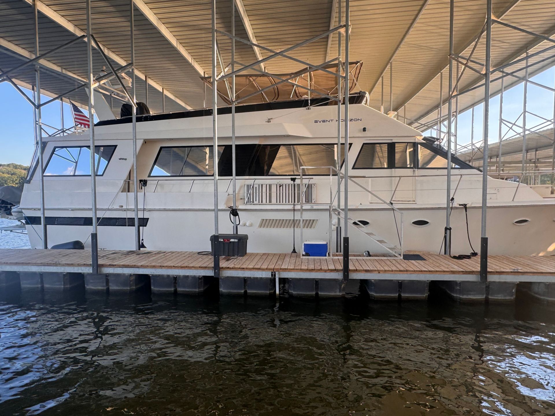 White yacht docked under a covered pier, black accents. Water surrounds the dock.