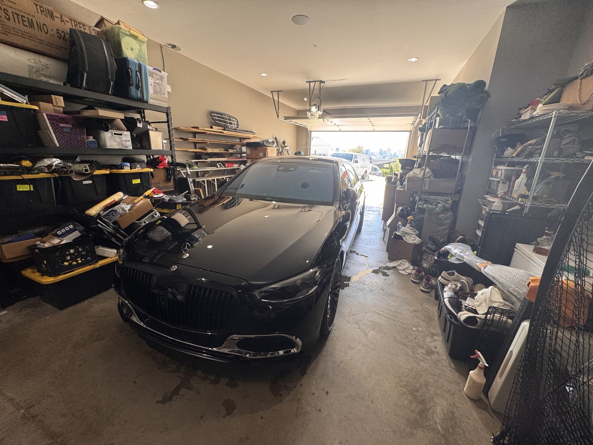 Black car parked in cluttered garage. Shelves and piles of items surround the car.