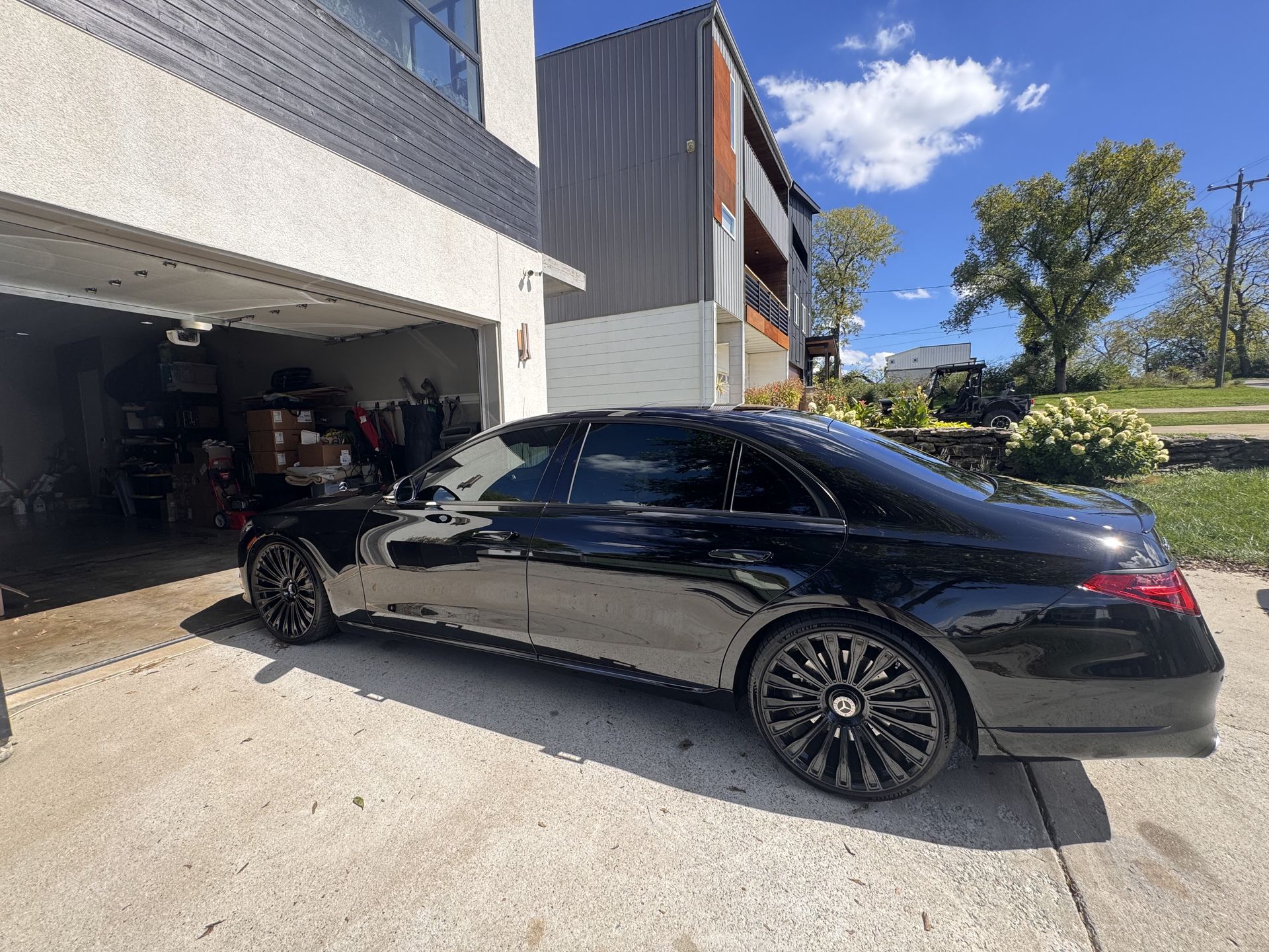 Black car parked in front of a garage and house on a sunny day.