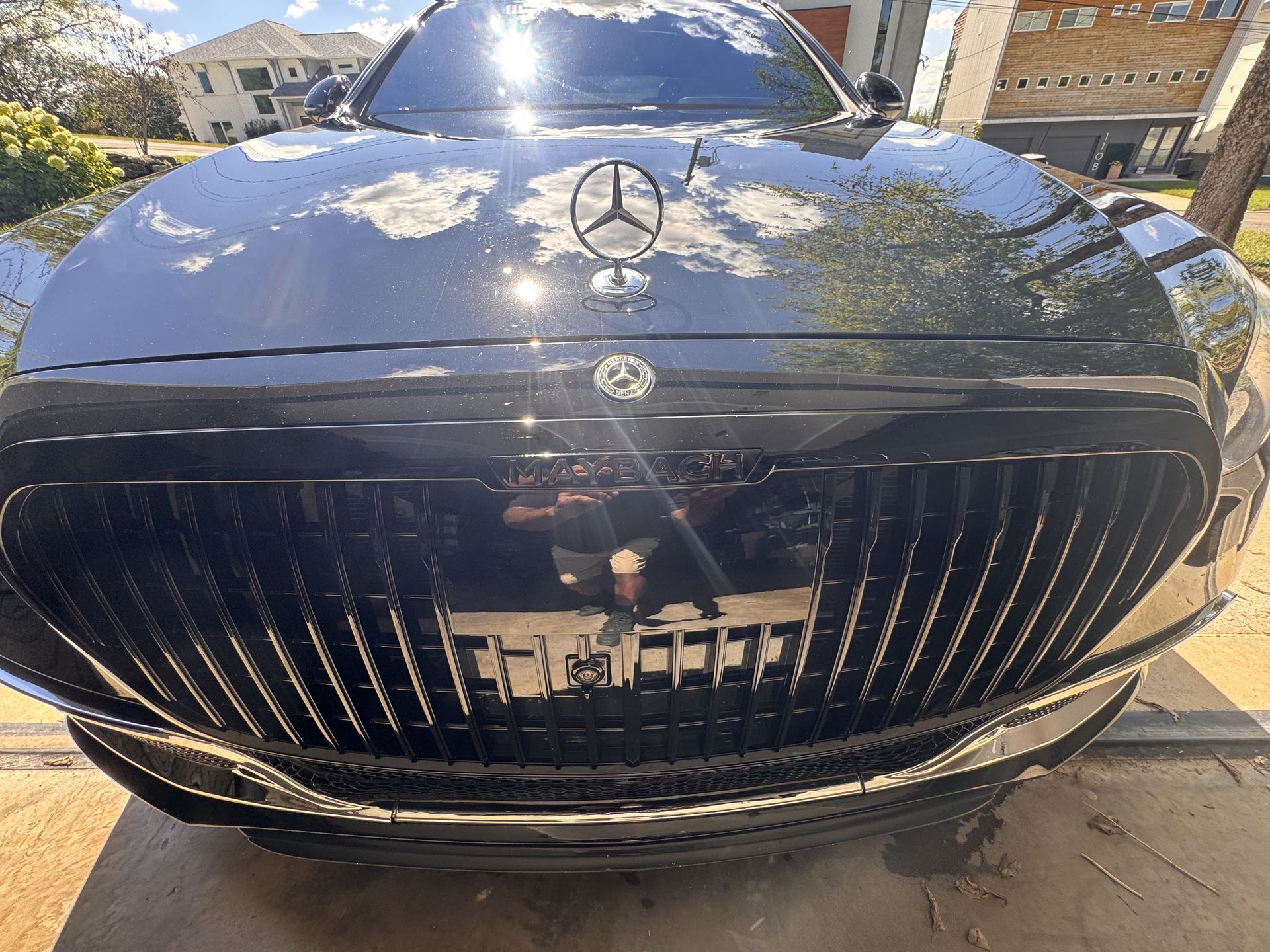 Black Mercedes-Maybach car's front grille with the Mercedes logo, in a driveway setting on a sunny day.