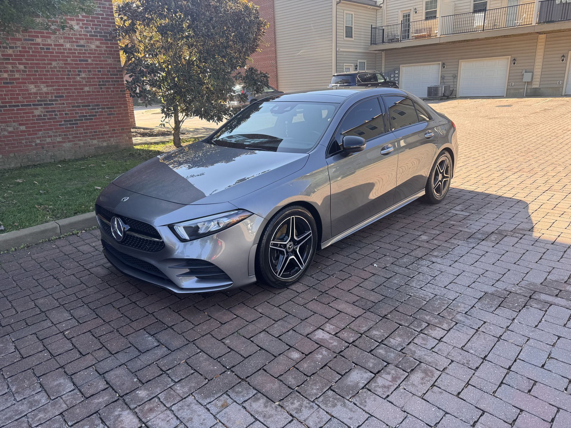 Gray Mercedes-Benz sedan parked on brick pavers in front of a building.