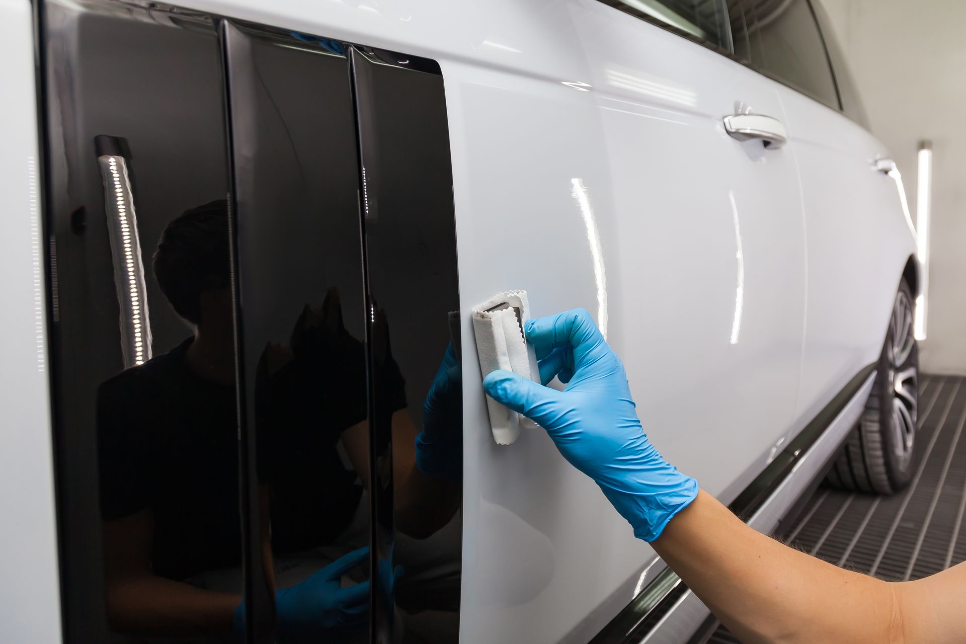 Gloved hand applying coating to a car door. White car in a garage, black trim, shiny surface.