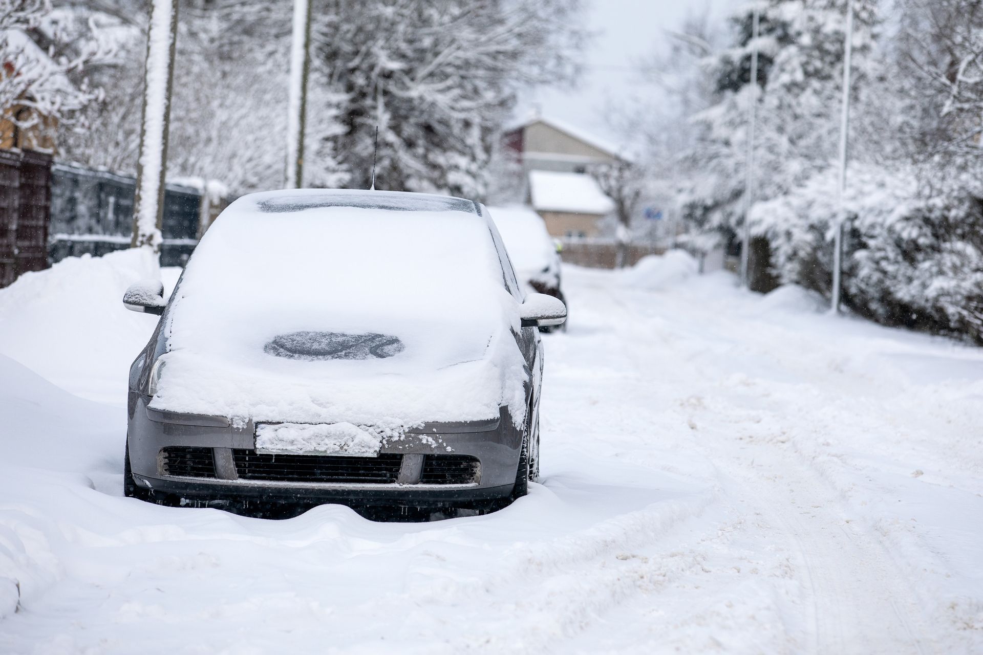 Gray car covered in snow parked on snow-covered street in a residential area.