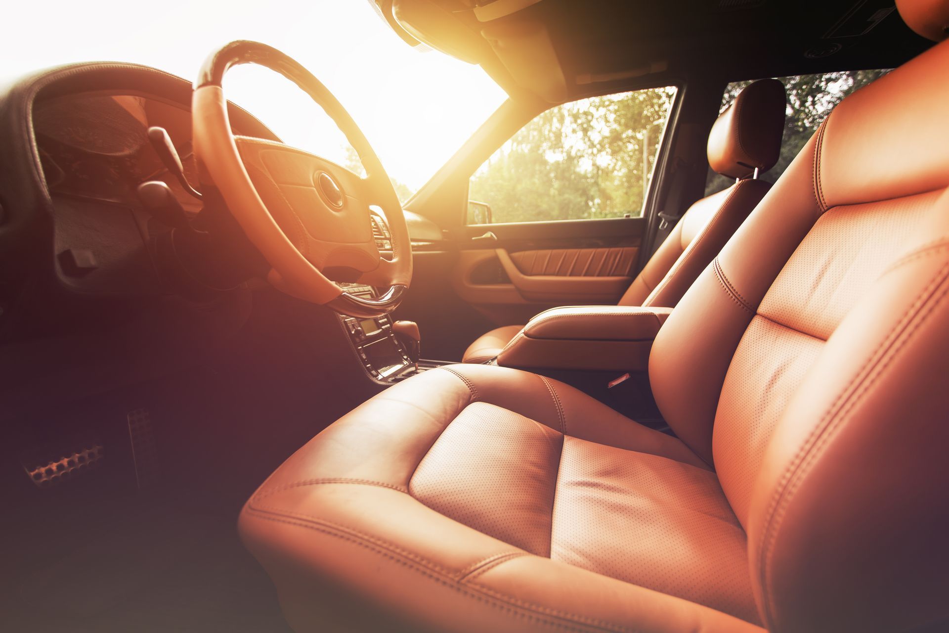 Interior of a car with brown leather seats and steering wheel, lit by sunlight.