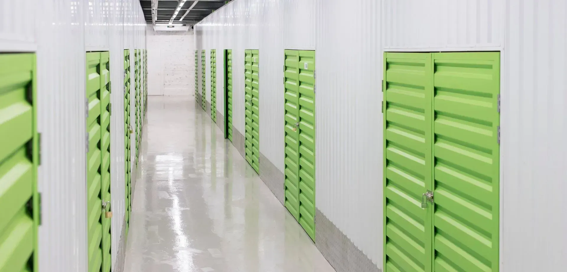 A long hallway with green doors in a storage facility.
