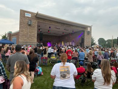 Two riders on horses posing in front of a white barn. One rider wears a green shirt, the other a black coat.