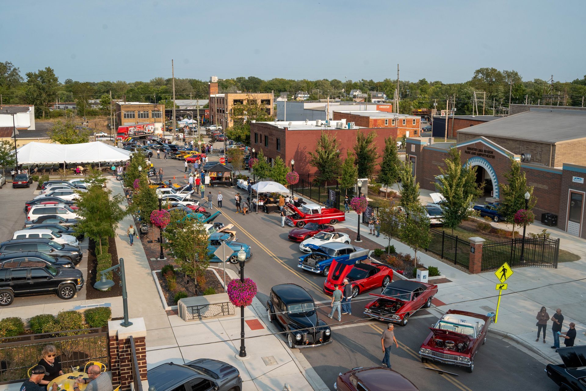 An aerial view of a car show with various classic and modern vehicles parked along a downtown street.