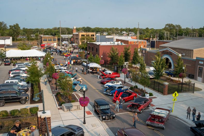 A car show takes place on a street lined with historic brick buildings and trees, with many classic cars on display.