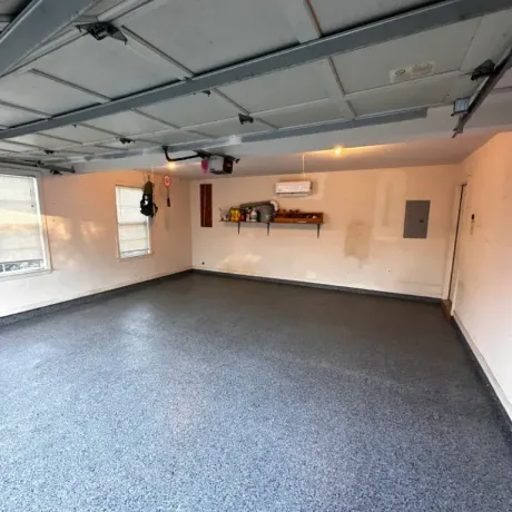 Empty garage with a gray speckled floor and white walls.