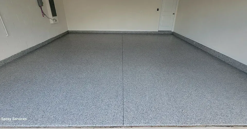 A garage with a gray speckled epoxy floor, bordered with gray trim, and white walls.