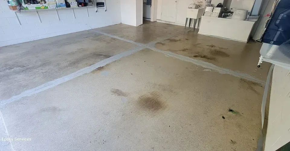 Garage floor with gray concrete and lighter lines, stained in spots.