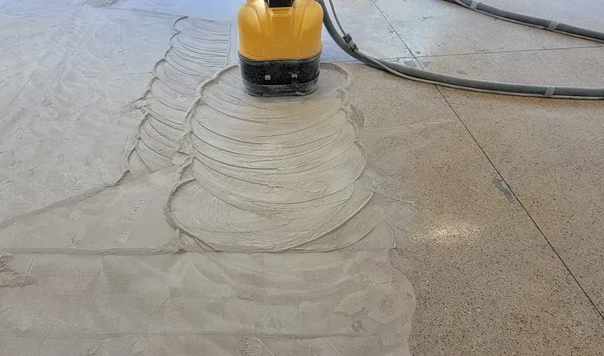 A machine grinding concrete floor, creating circular patterns in the gray cement.